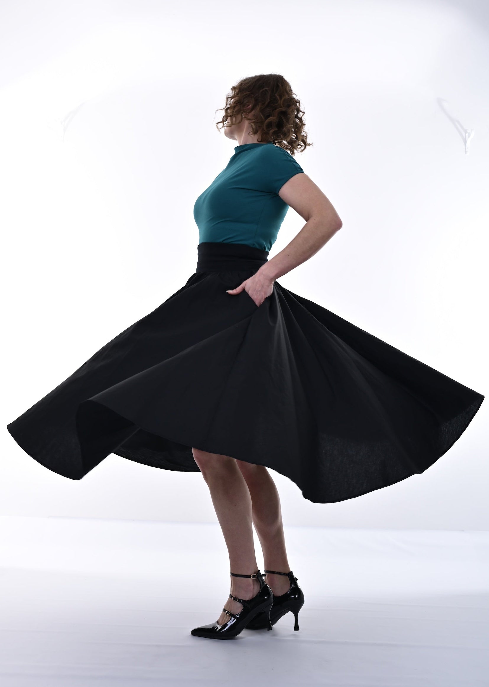 Person wearing a black skirt and teal top, standing against a white background