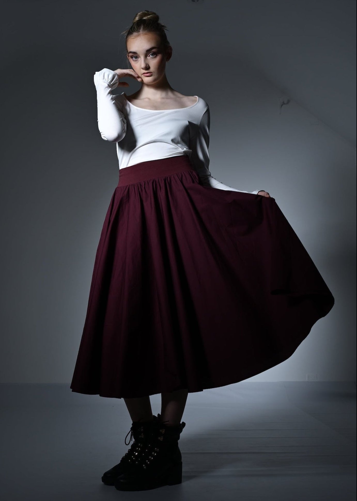 Woman wearing a white top and burgundy skirt with gloves in a studio setting