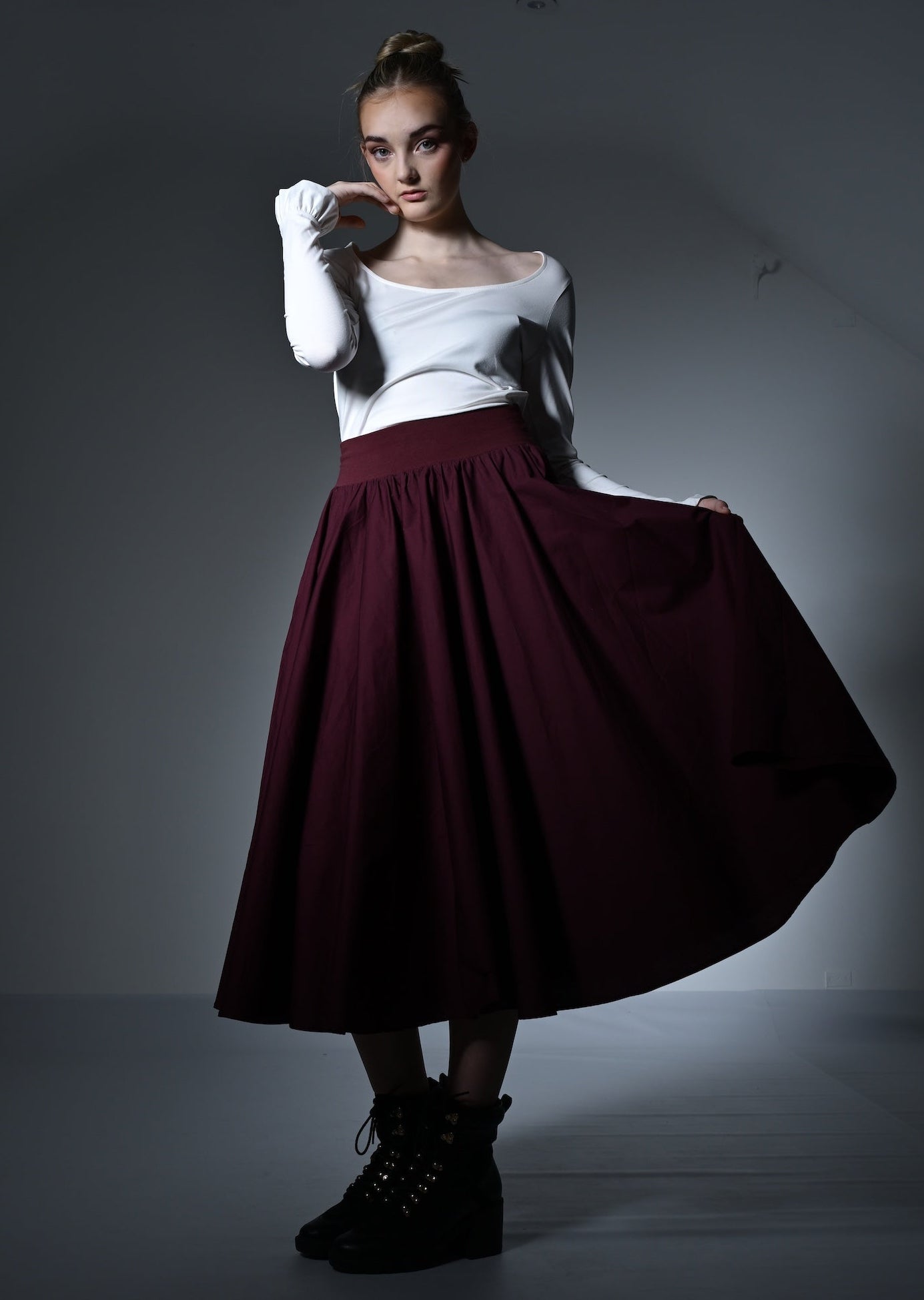 Woman wearing a white top and burgundy skirt with gloves in a studio setting