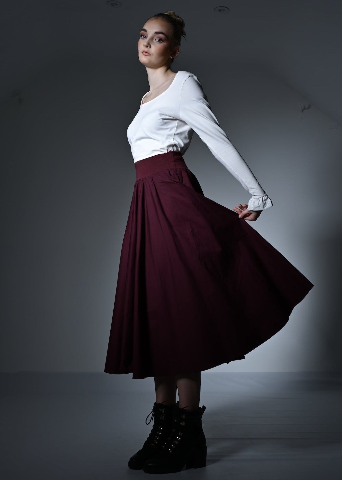 Woman in a white top and burgundy skirt posing against a plain background