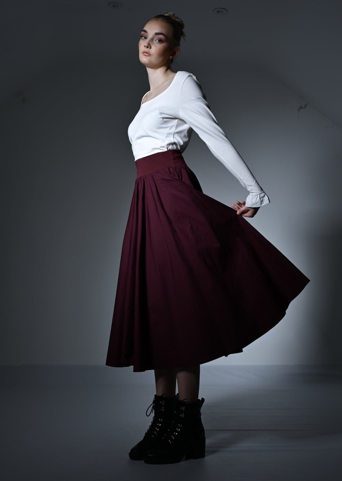 Woman in a white top and burgundy skirt posing against a plain background