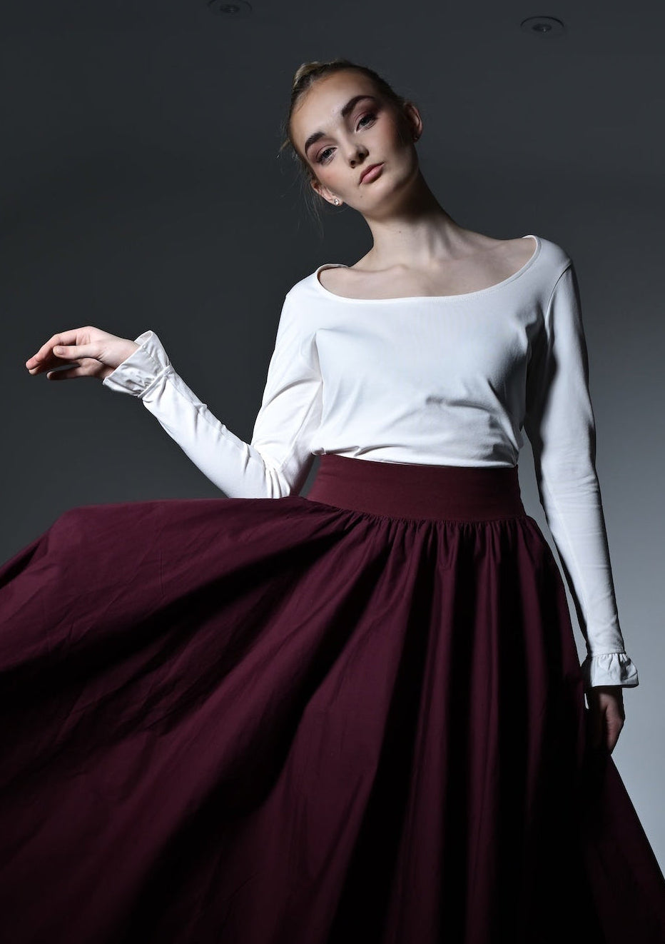 Woman in a white top and burgundy skirt posing in a dark room.