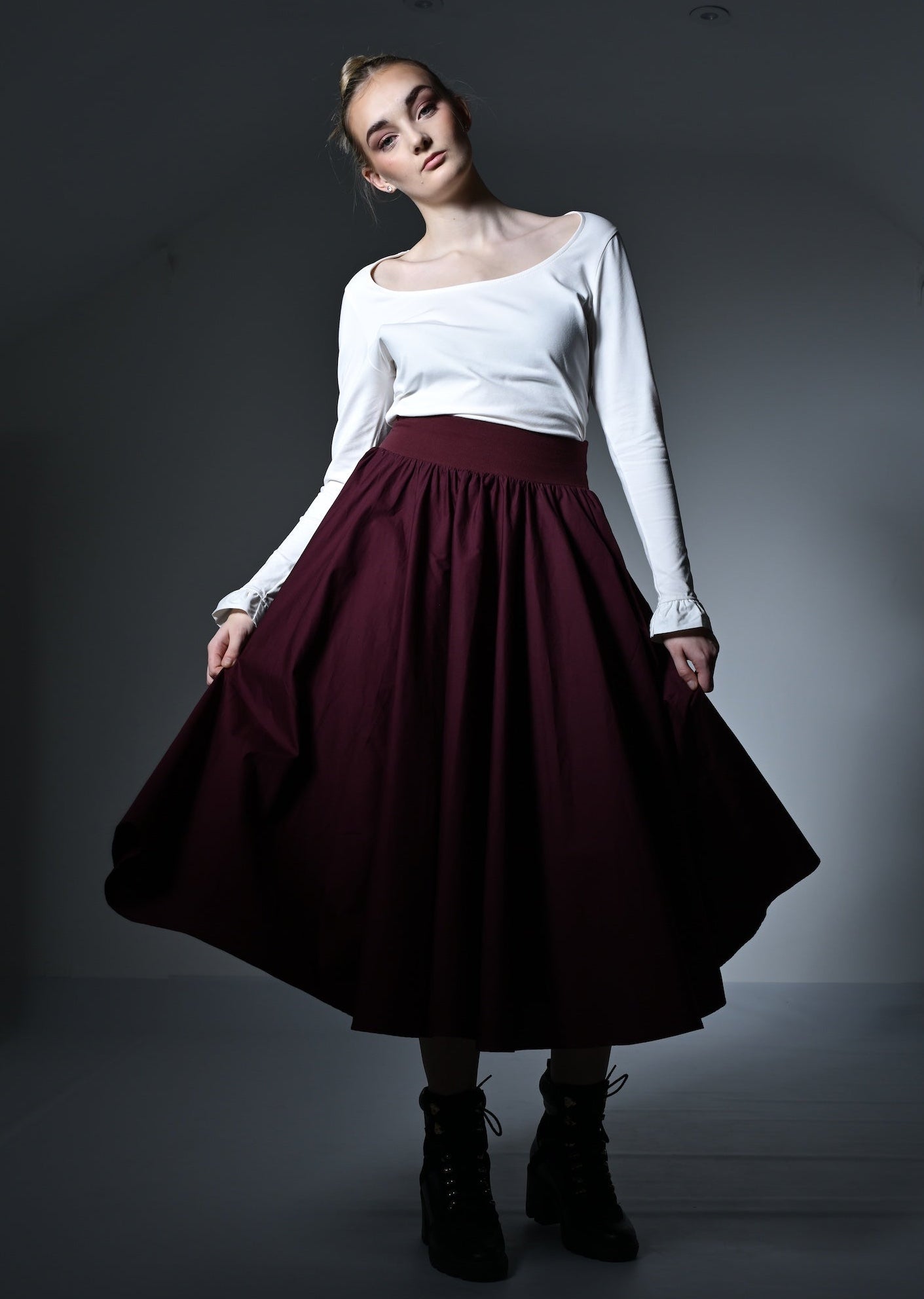 Person wearing a white top and burgundy skirt in a dark room