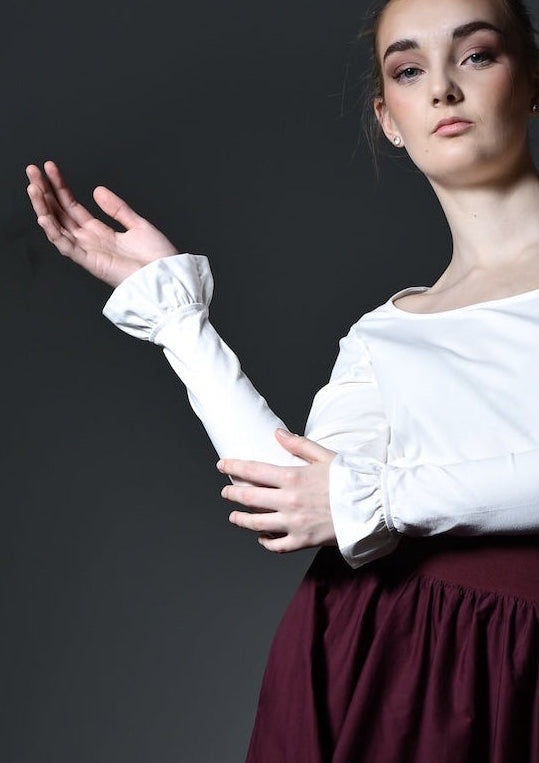 Woman in a white top and burgundy skirt standing against a dark background