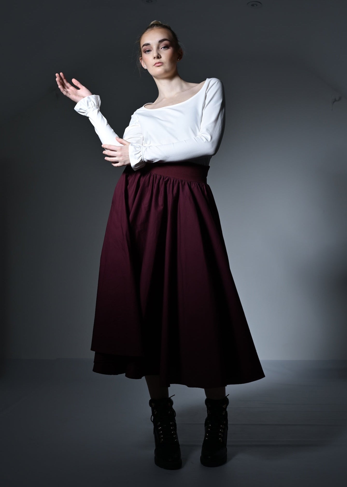 Woman in a white top and burgundy skirt posing against a dark background