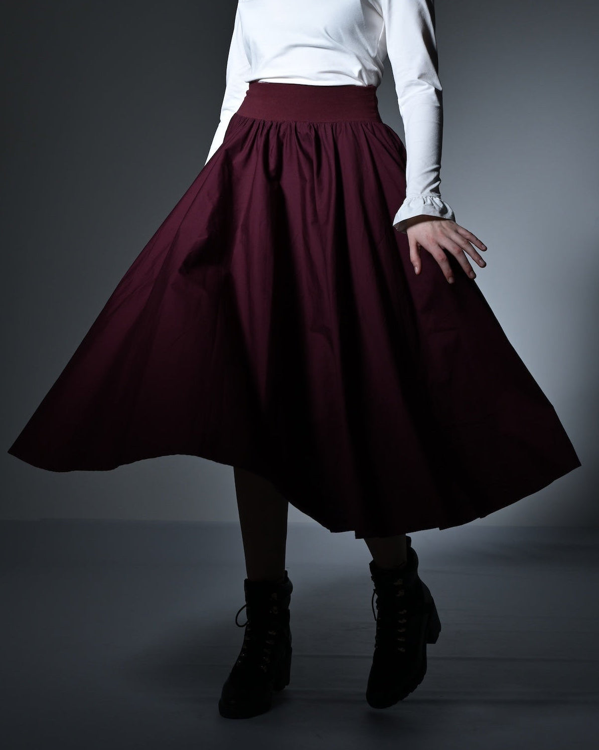 Woman wearing a white top and burgundy skirt in a dimly lit room