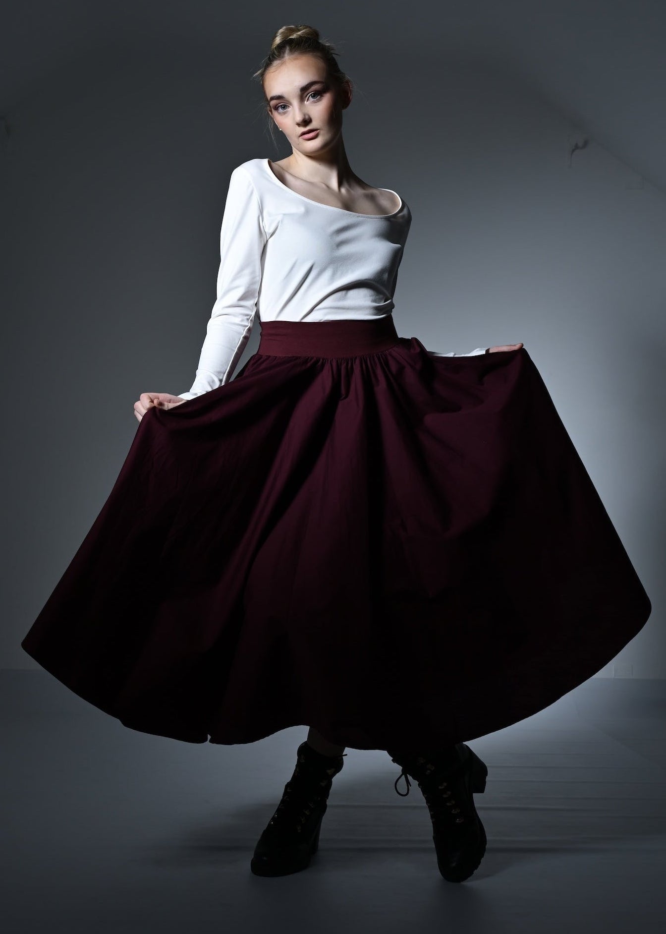 Woman wearing a white top and burgundy skirt in a dimly lit room
