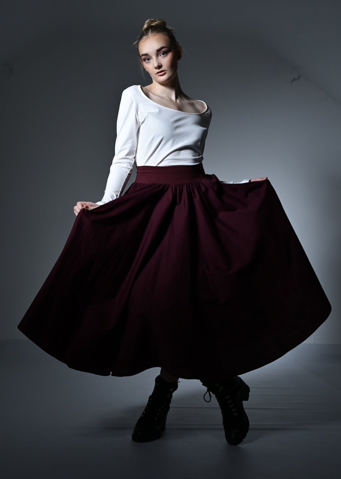 Woman wearing a white top and burgundy skirt in a dimly lit room