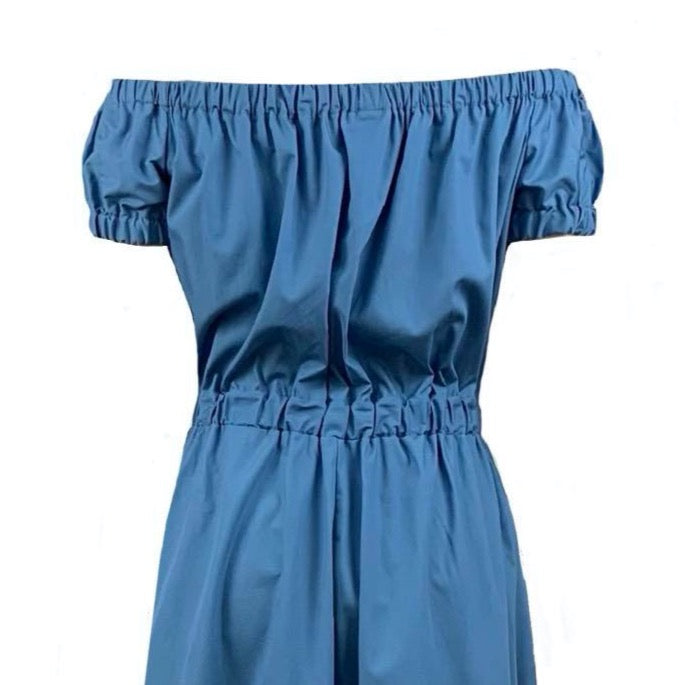 This is the top of a Bardot style dress in wedgwood blue silhouetted against a white background. The neckline is gathered and the sleeves are a small puff style. The top gathers in to the waist elastic and the skirt is full with side pockets. 