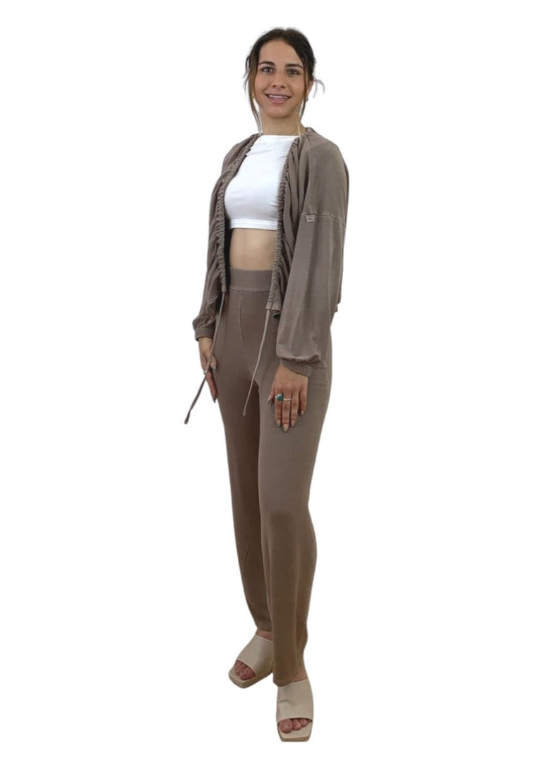 This is a young lady with dark hair wearing a white crop top. She is silhouetted against a white background and faces the camera. She is wearing a mocha cardigan and mocha trousers.