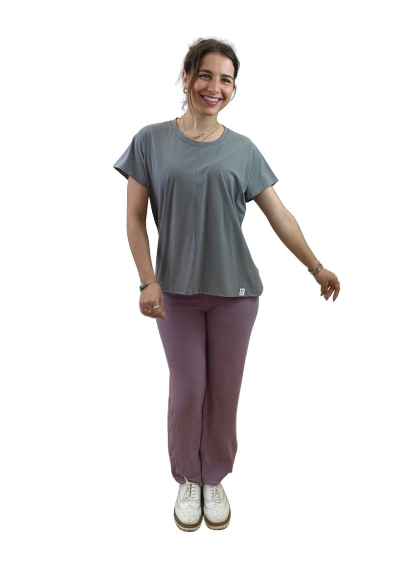 This is a young lady with dark hair wearing a grey T shirt. She is silhouetted against a white background and is facing the camera with her left arm outstretched. She is wearing pale grape trousers with white shoes.