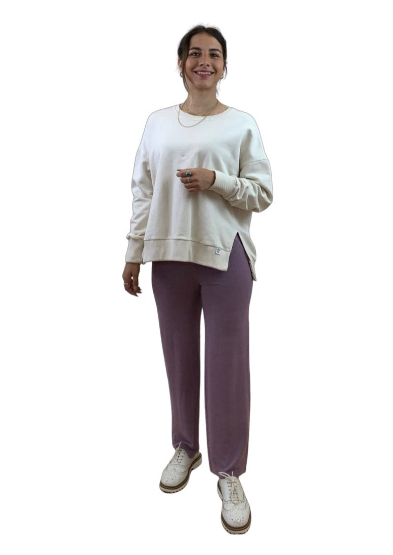 This is a young lady with dark hair wearing a long sleeve white top. She is silhouetted against a white background and is facing the camera. She is wearing pale grape trousers with white shoes.